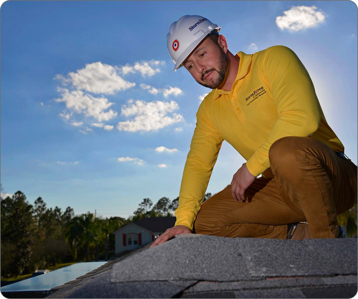 A professional roofer from StormForce in a white helmet and yellow shirt is carefully inspecting a shingle rooftop. 