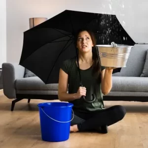 Woman sitting on the floor with an umbrella to avoid a leaking roof